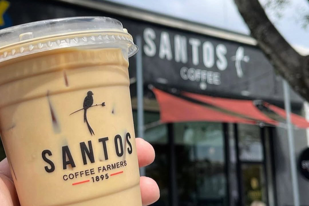 Iced coffee cup with the Santos Coffee Farmers logo held outside the Santos Coffee shop in Birmingham, Alabama, showcasing Guatemalan specialty coffee.