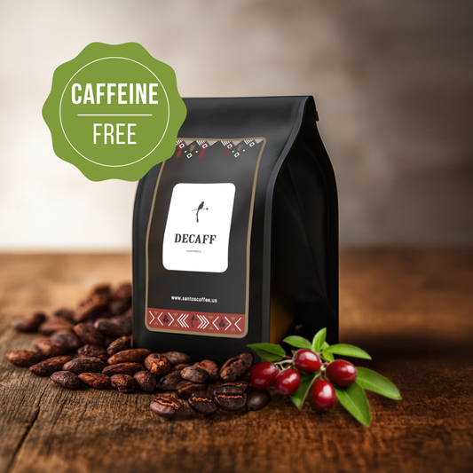 Santos Coffee Decaf Coffee bag labeled “Caffeine Free,” surrounded by roasted coffee beans and fresh coffee cherries on a wooden table.