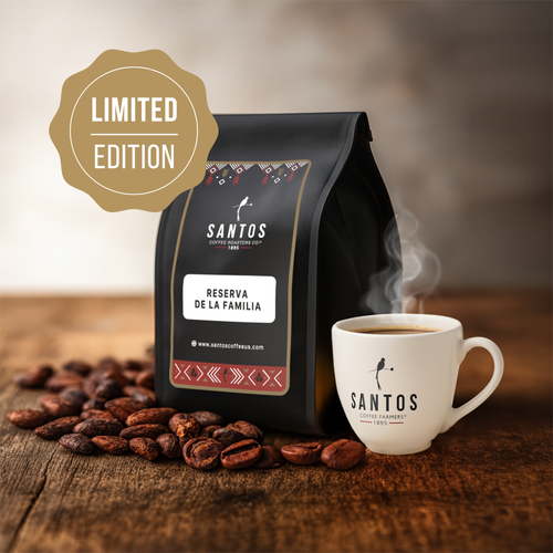 Santos Coffee Reserva de la Familia Limited Edition coffee bag beside a steaming cup of coffee and scattered beans on a rustic wooden table.