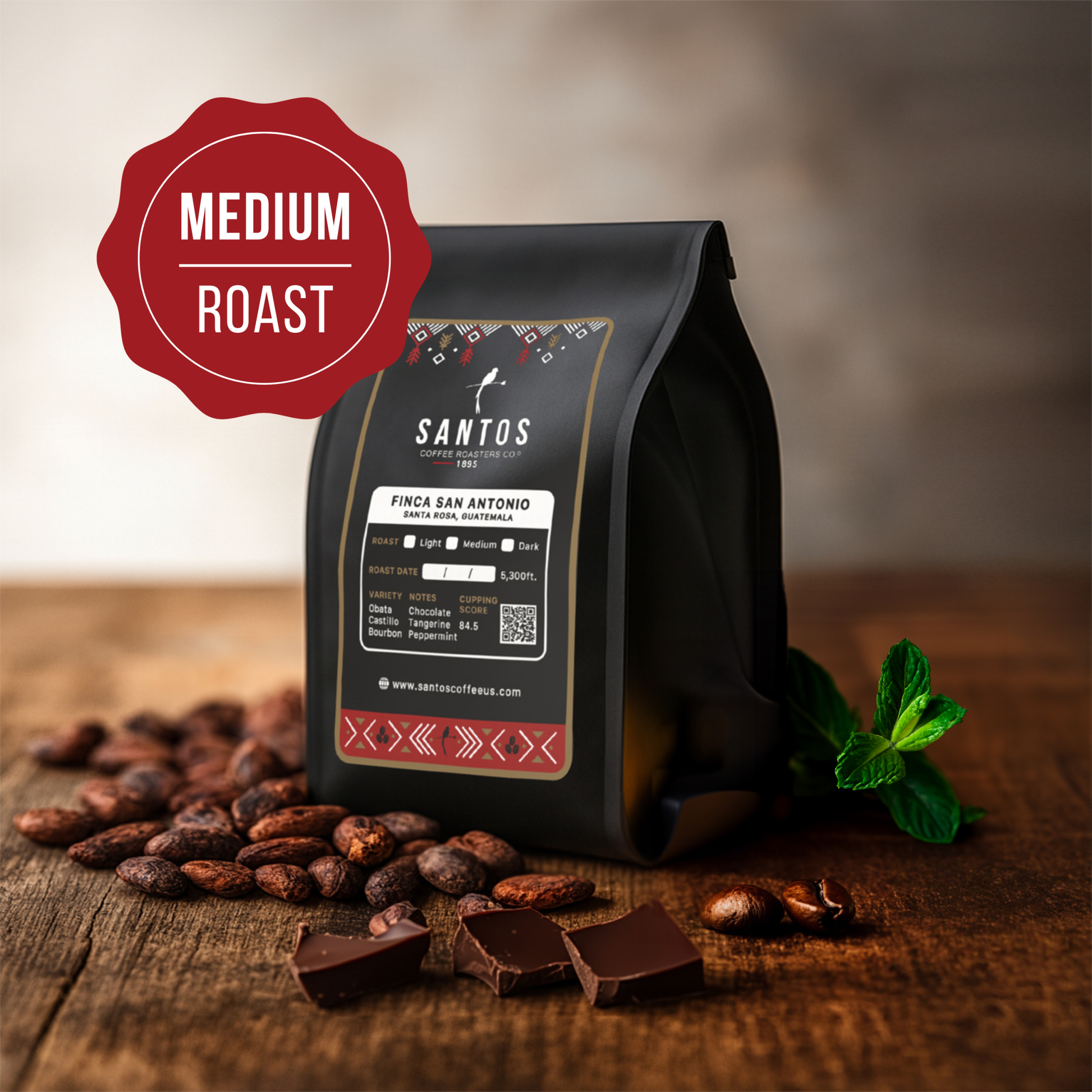 Santos Coffee San Antonio Medium roast coffee bag, surrounded by cocoa beans, chocolate pieces, and fresh mint leaves on a rustic wooden table.